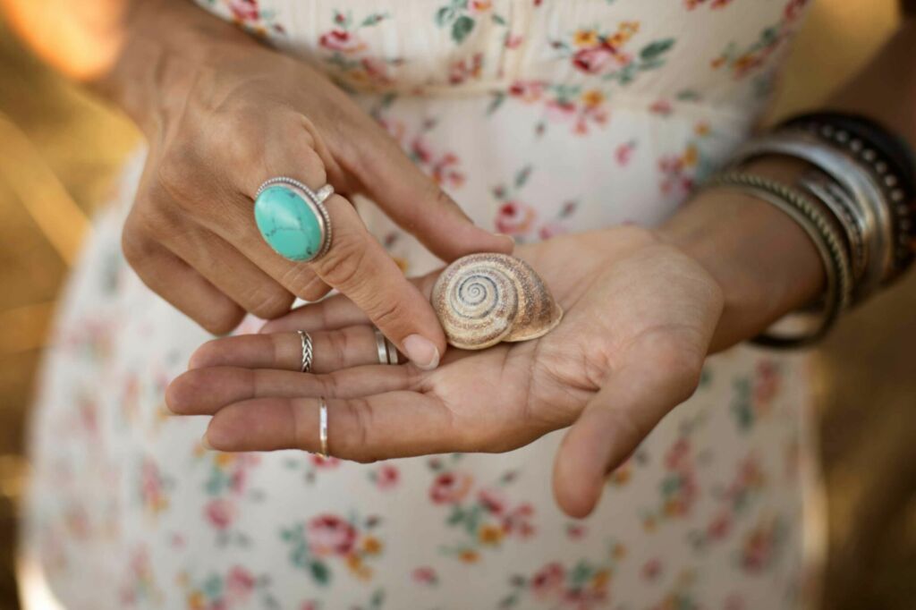Mãos femininas segurando uma concha, representando a essência da Sirenar.art – joias artesanais e semijoias inspiradas no mar, naforça das pedras e cristais e na natureza.