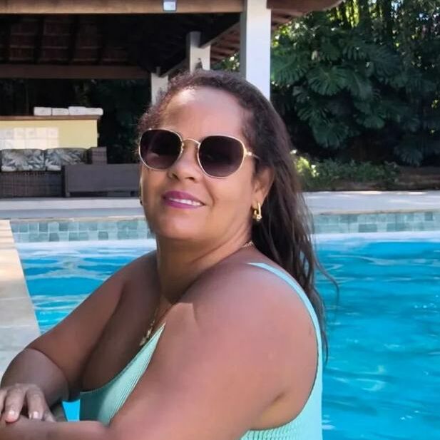 Elis posando de óculos escuros e roupa verde junto à piscina